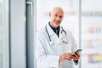 Male doctor using mobile phone while standing on the hospital's foyer