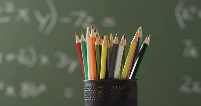 Video of cup with crayons on wooden table over mathematical formulas on blackboard