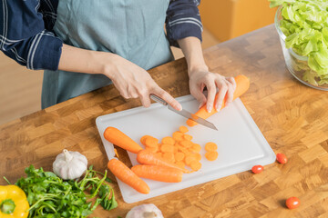 Asian young woman, girl or housewife hand using knife, cutting carrots on  board, on wooden table in kitchen home, preparing ingredient, recipe fresh vegetables for cooking meal. Healthy food people.