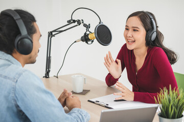 Naklejka premium Smile two asian young woman, man radio hosts in headphones, microphone while talk, conversation, recording podcast in broadcasting at studio together. Technology of making record audio concept.