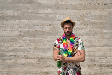Young and handsome man, blue eyes, with beard, hat, Hawaiian shirt and flower necklace with arms...