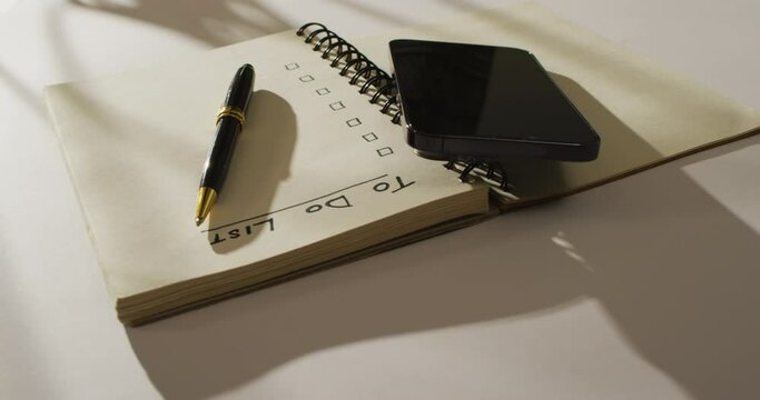 Video of notebook with to do list and copy space, smartphone and pen on wooden surface