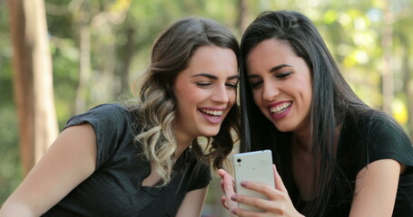 Authentic friends together outdoors checking cellphone Girls looking and holding smartphone chatting exchanging gossip