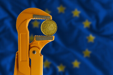 20 euro cent coin held in an orange plumber wrench on the background of the European Flag. Obverse...