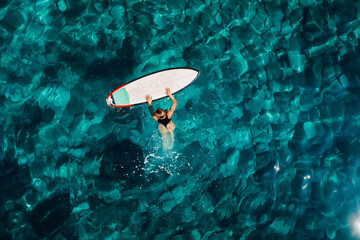 Surf girl swim with surfboard in transparent ocean. Aerial view
