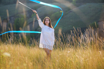 A teenage girl with a gymnastic ribbon on a hillside.