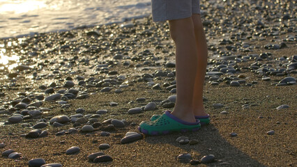 Waves on pebbled beach during sunset. Creative. Vacation Concept, side view of a boy legs standing at the sea shore.
