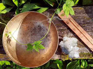 Singing bowl with quartz crystal, incense and green leaves on a wooden background, musical...