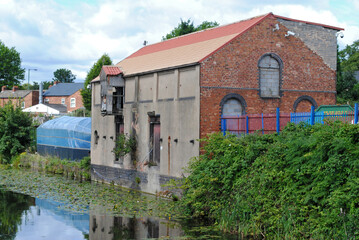 Fototapeta na wymiar Old Industrial Mill Building beside Still Waters of Canal 