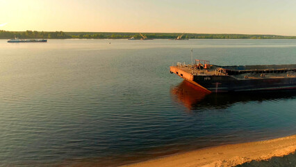 Cargo barge moored by the river shore on clear sky background. Scene. Concept of water transport.