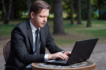 Focused businessman. Attractive young man in formalwear working on laptop while sitting at the table outdoors.