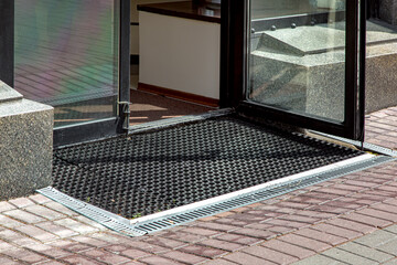 descent on entrance to store from pedestrian sidewalk with rubber foot mat with gray storm drain lattice, granite facade of stone exterior of building close-up, lit by sun side view nobody.