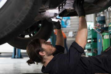 Mechanic maintenance underneath lifted car. Technician vehicle service checking under car at...