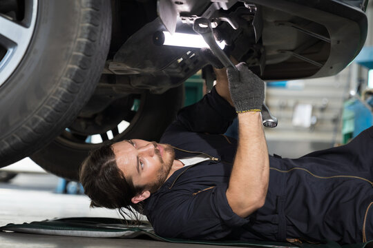 Mechanic maintenance underneath lifted car. Technician vehicle service checking under car at automotive motor garage