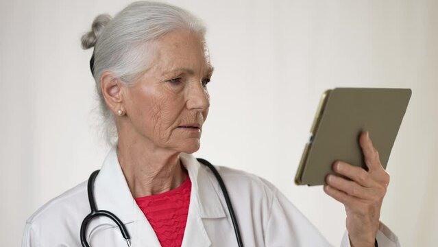 Pretty senior, elderly, mature woman doctor making video call with patient, on smartphone tele health, telemedicine concept on tablet computer