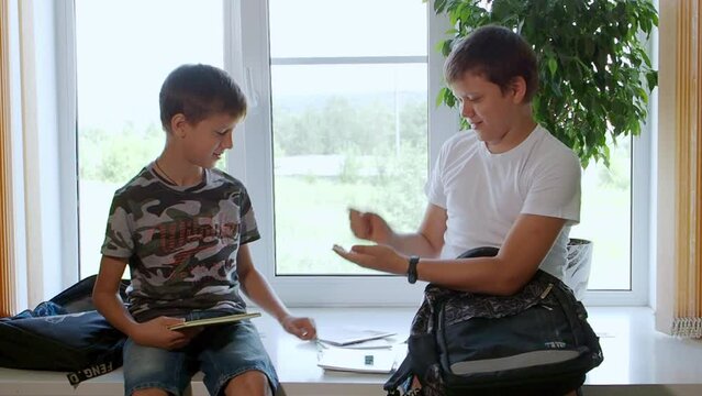 Two boys are going to school and choosing stationery, washing. Boys schoolchildren check textbooks in a school backpack at home before school. They sit on top of table at home. Back to school.