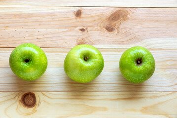 Flat lay photo of fruits. Three green, ripe and tasty apples on a natural wood background
