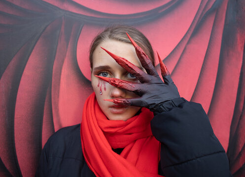 Halloween girl portrait. Beautiful girl with Halloween make-up and handmade gloves with bloody clowes in red scarf against the background of wall painted with graffiti in red and black colors