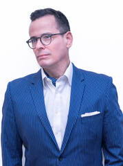 Half body shot of a distinguished looking 40-something man with dark hair and stylish eyeglasses wearing a blue blazer with a pocket square and ascot. © TODDGRANT