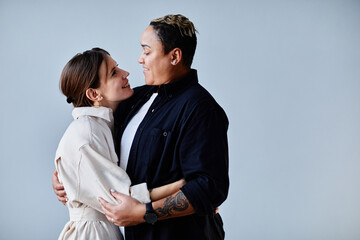Minimal side view portrait of happy gay couple embracing against blue background, copy space