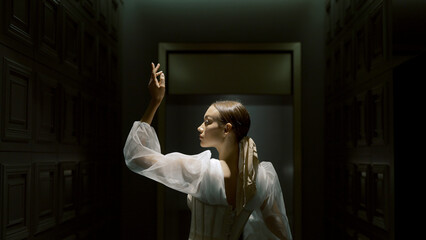 Mysterious woman in white dress and dark place. Action. Attractive and mysterious woman with dim light. Beautiful woman in white dress posing