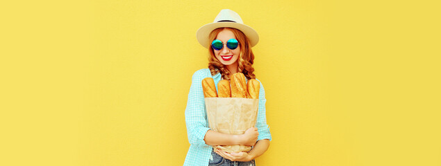 Portrait of happy smiling young woman holding grocery shopping paper bag with long white bread baguette on yellow background