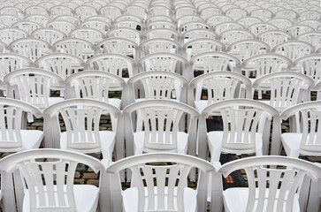 Seemingly endless number of rows of white plastic chairs in an outdoor setting