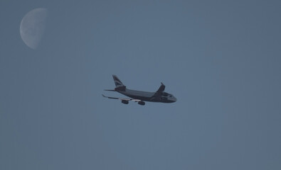 Passenger airliner flying in the evening sky. Large incomplete moon. Travel and change of area of...