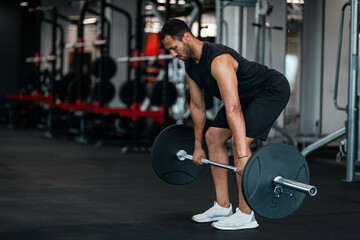 Obraz na płótnie Canvas Sporty Black Man Lifting Heavy Barbell While Training At Gym