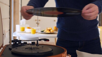 A man puts a vinyl record into a player and turns it on. The record spins and the man lowers the needle to read the music. Listening to music at home alone, classical music from the gramophone.
