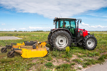 Wheeled tractor with rotary mower in the field next to the road