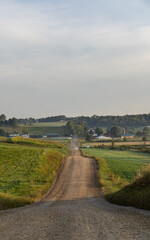 Fototapeta na wymiar Straight dirt road cutting through the hilly fields of Ohio's Amish country | Back road in rural America