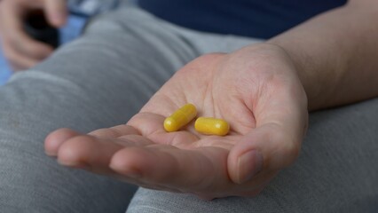 Two gelatin capsules with medicines are poured into the palm of your hand. Yellow capsules with drugs for the treatment of serious diseases. The high price of drugs and medicines.