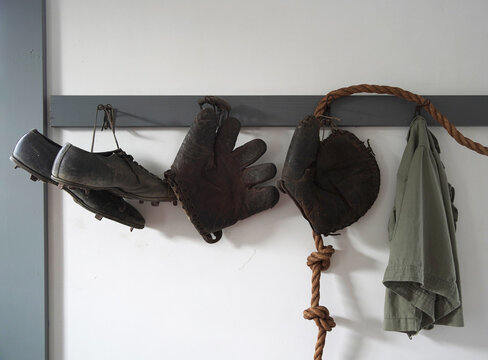 Old Fashioned Catchers Mitt, Baseball Glove, And Pair Of Cleats Hanging On A Wall In The School