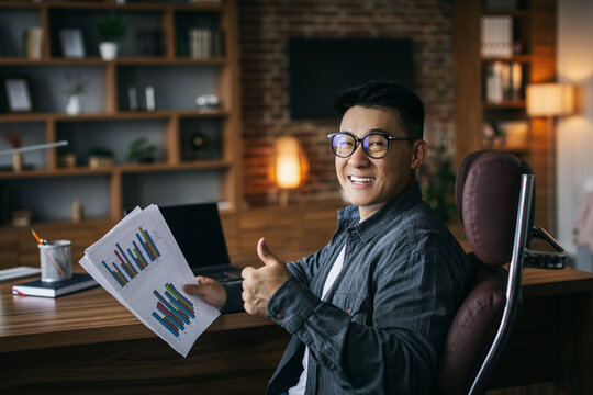 Happy Adult Asian Businessman In Glasses Working With Charts And Showing Thumb Up, Thinking About Online Project