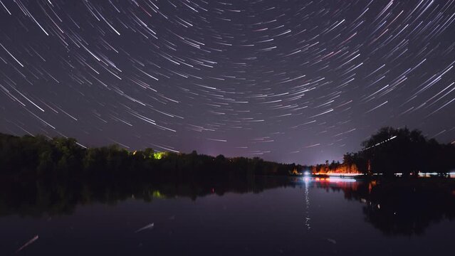 Stars rotate to become star trails over river with traffic light pollution on the road at a distance