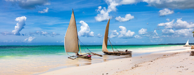 Dhows an einem Strand auf Sansibar. Boote im türkisfarbenen Ozean und blauer Himmel in Tansania, Panorama. - obrazy, fototapety, plakaty