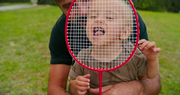 Happy Young father have fun with cute son enjoying nature together. Playing with tennis racket in park.