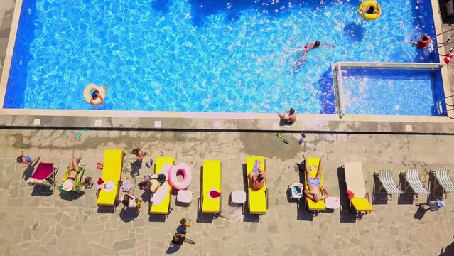 Aerial view from flying drone of people having fun, playing and resting in water in pool. kurt or villa with vacationers. Party of friends or celebration. Sun beds and young people sunbathe in sun.