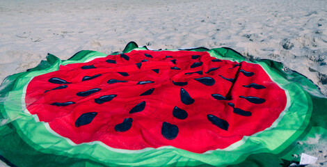 watermelon print towel is on the sand. Beach in the background blurred