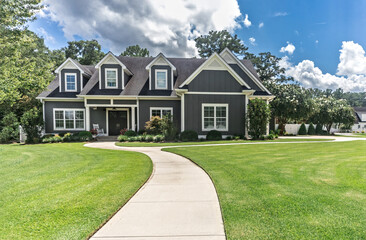 A large gray craftsman new construction house with a landscaped yard and leading pathway sidewalk