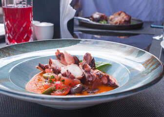 Fried octopus in tomato sauce with olives and capers in a blue plate. Delicious traditional Italian dish. Dinner at a fish restaurant.