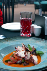 Fried octopus in tomato sauce with olives and capers in a blue plate. Delicious traditional Italian dish. Dinner at a fish restaurant.