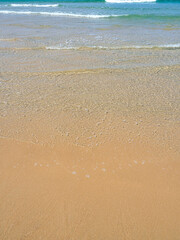 Picturesque beach scenery on the coast of Cadiz, Spain. Orange sand, turquoise sea with waves and foam, clear sky, vacation, summer, relax.