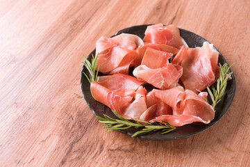 Charcuterie plate with proscuitto served with olives at wooden table background with copy space. Black plate with traditional italian antipasti. Selective focus