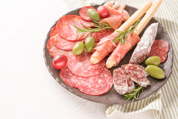 Charcuterie plate with variery of sausages - salami, bresaola, proscuitto served with olives and grissini over white table. Menu background with copy space. Traditional italian antipasti