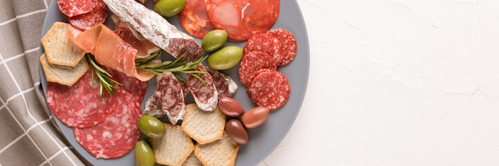 Banner with assortment of different meat snacks, charcuterie plate with different types of sausages. Gray plate with traditional italian antipasti on white table with copy space