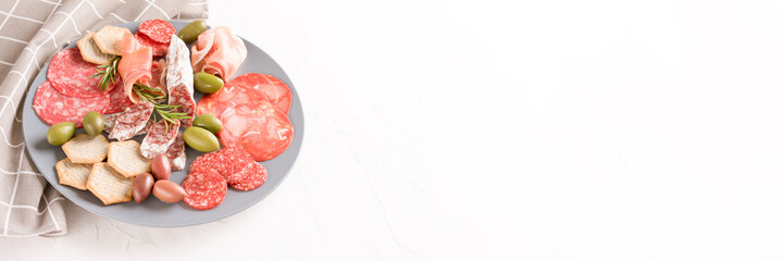 Assortment of different meat snacks, charcuterie plate with different types of sausages. Gray plate with traditional italian antipasti on white table with copy space. Banner