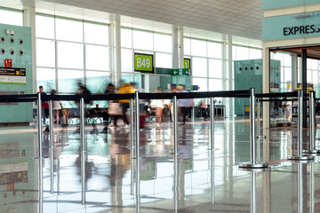 Empty waiting lines at an airport terminal as passengers walk by in motion blur in Barcelona, Spain.