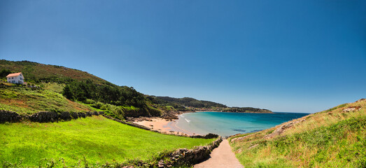 Panoramic photo of a beach with crystal clear water and a house and vegetation (Porto do Son, Galicia)